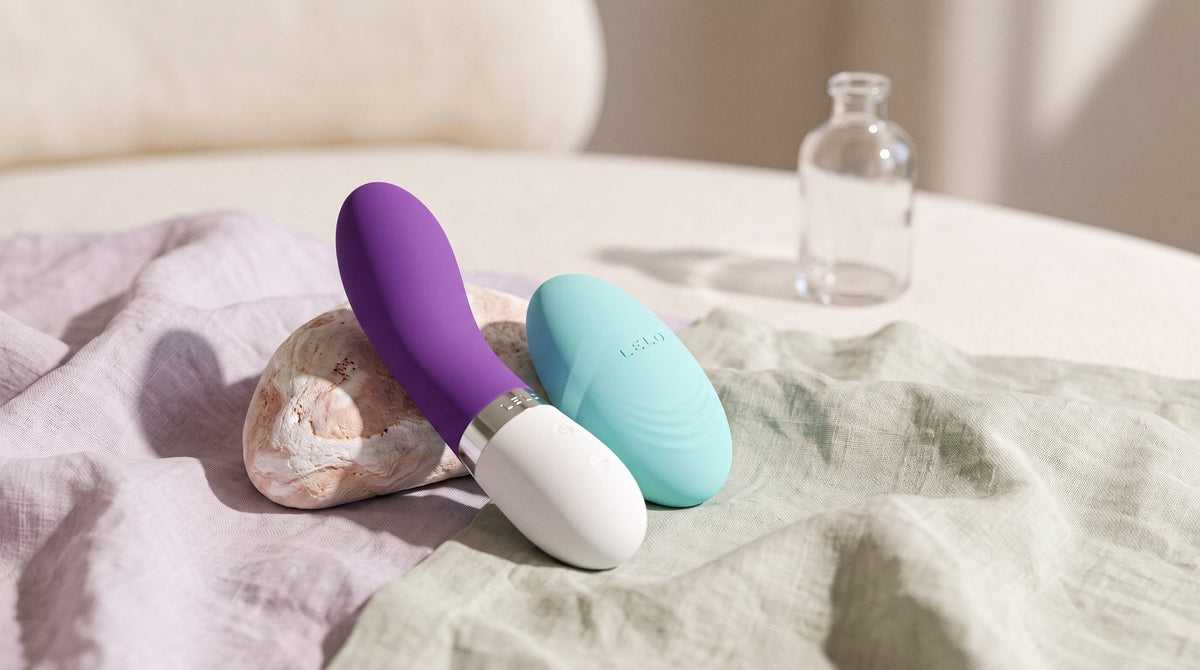 Vibromasseurs LELO Gigi 3 et LELO Lily 3 posés côte à côte sur un lin naturel froissé, près d’une pierre claire, en lumière douce