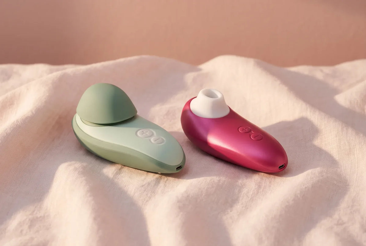 Deux stimulateurs Womanizer posés sur du lin ivoire.