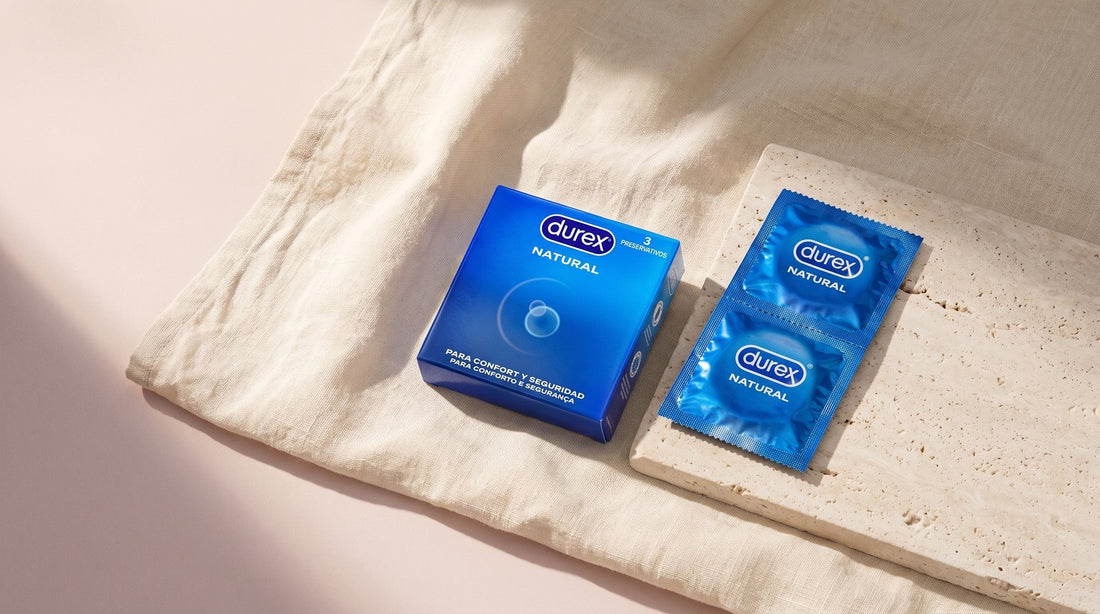 Boîte de préservatifs Durex Natural posée sur un lin écru, avec deux sachets individuels scellés alignés sur une pierre claire