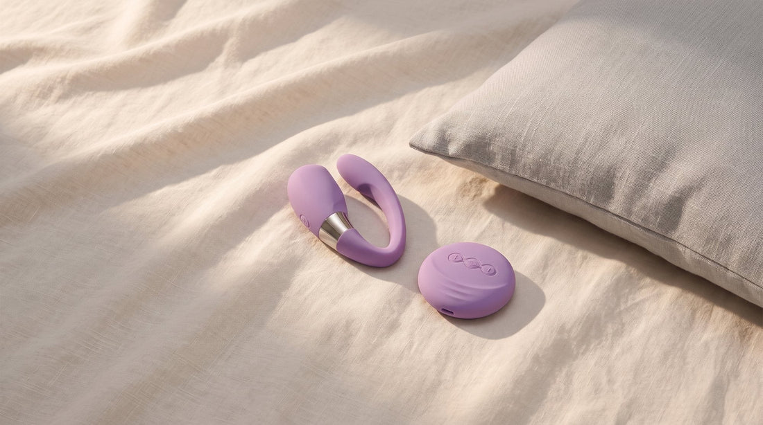 Lila Paarvibrator LELO Tiani 3 auf hellem, leicht zerknittertem Leinenlaken neben einem grauen Kissen im weichen Seitenlicht