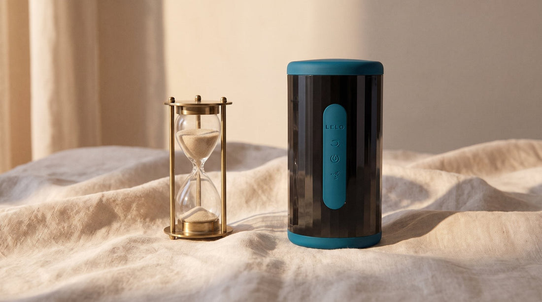 Masturbador LELO F2S Double Sonic azul petróleo de pie sobre una sábana de lino crudo, junto a un reloj de arena a medio vaciar