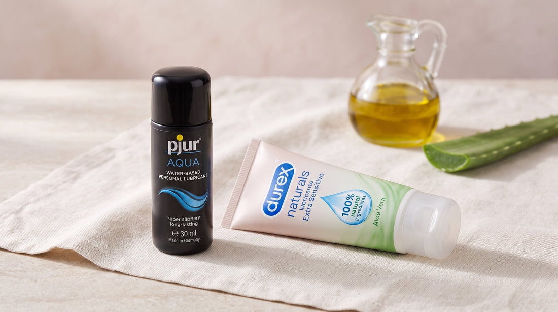 Flasche pjur AQUA 30 ml und Tube Durex Naturals mit Aloe vera auf hellem Stein, dahinter unscharf Olivenöl und ein Aloe-Blatt