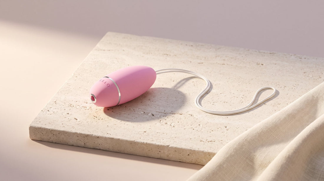 Liebeskugel LELO Luna Smart Bead mit sanft geschwungenem Rückholband auf heller Kalksteinplatte, am Bildrand ein Stück Leinen
