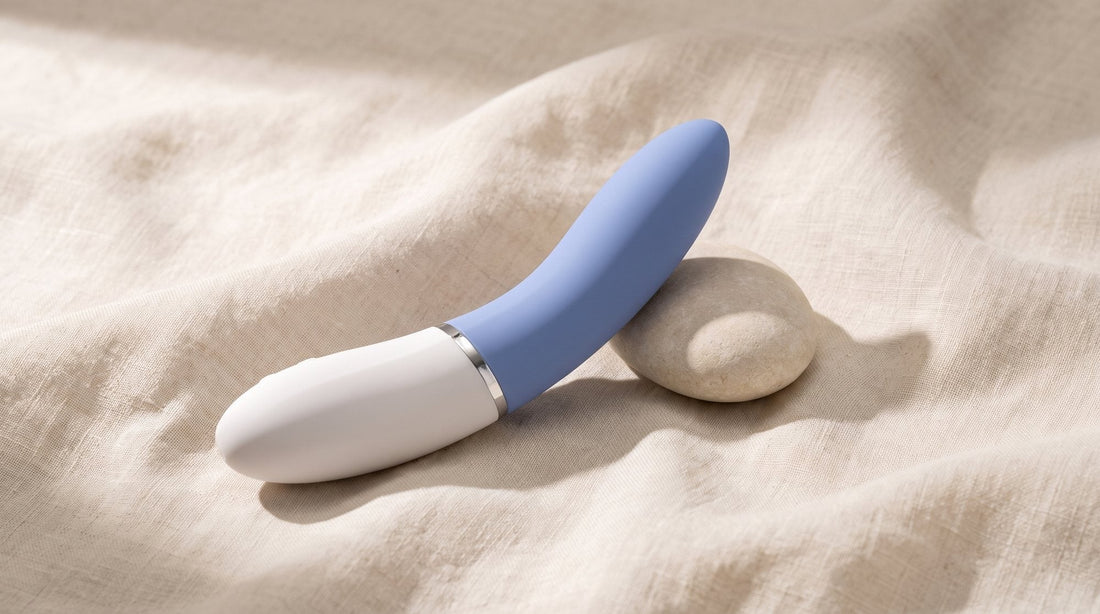 Vibromasseur point G LELO Liv 3 bleu posé en diagonale sur un lin écru froissé, près d’un galet clair, dans une lumière douce