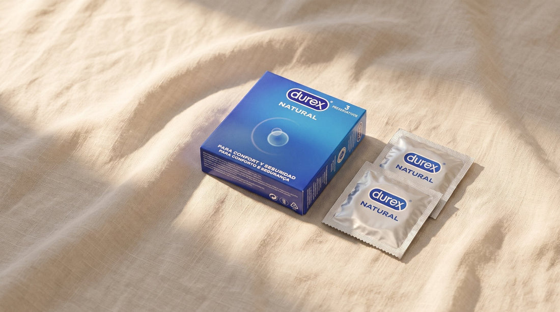 Caja de tres preservativos Durex Natural y dos sobres cerrados sobre un lino crudo, con luz suave de tarde
