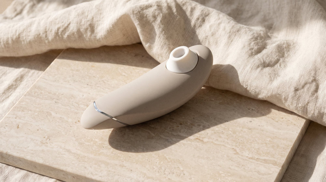 Stimulateur clitoridien Womanizer Premium 2 gris chaud posé sur une dalle de pierre claire, devant un pan de lin froissé