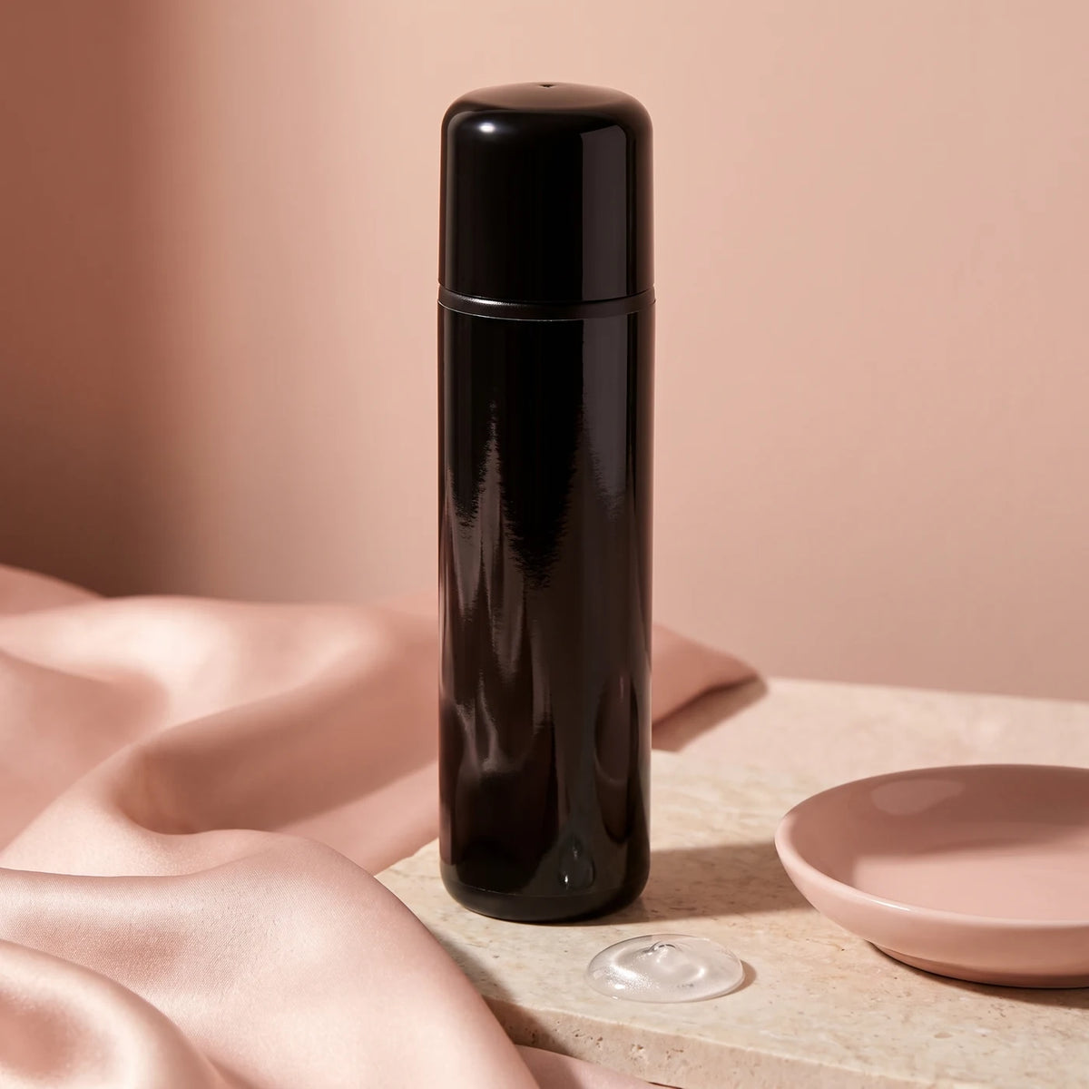Flasche pjur ORIGINAL Gleitgel auf Silikonbasis, von hinten, auf Satin in Blush neben einer Keramikschale.