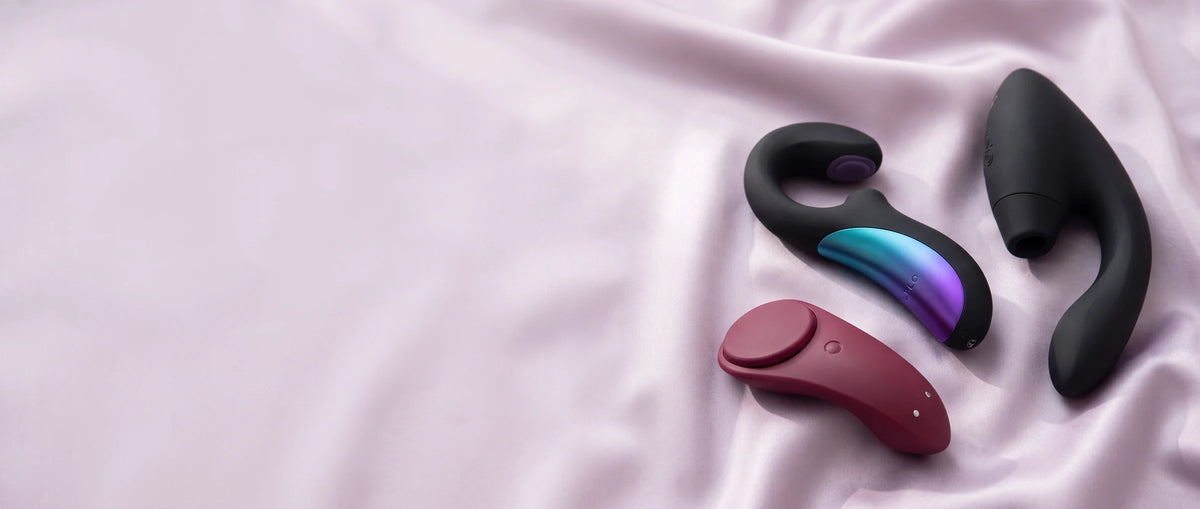 Womanizer Duo 2 y LELO Enigma Double Sonic negros y Satisfyer Sexy Secret burdeos sobre satén lila.