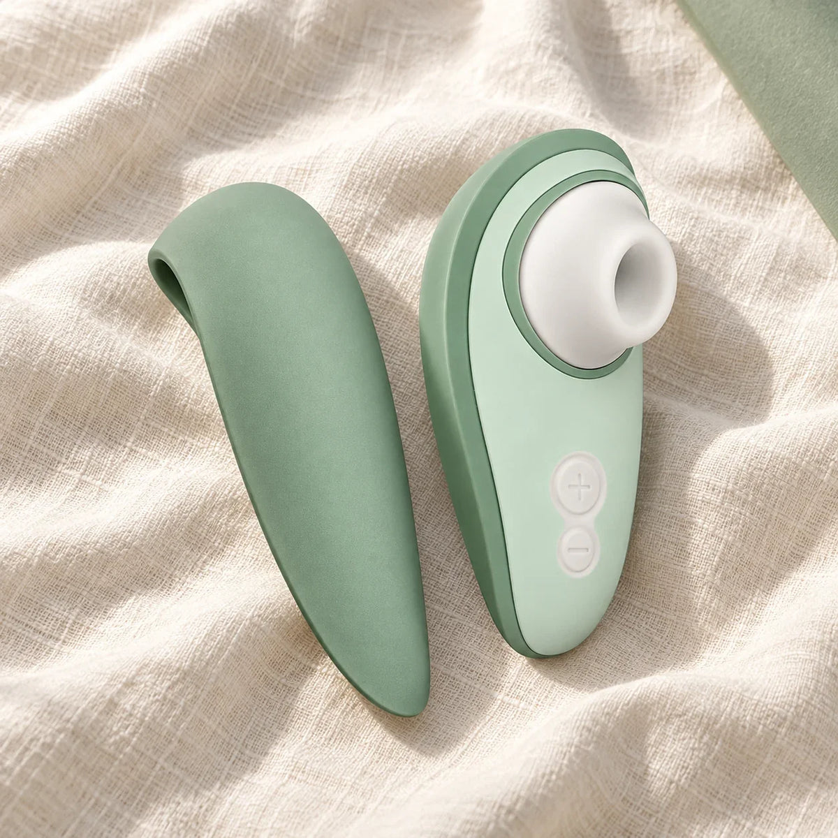 Womanizer Liberty 2 vert sauge et son capot de voyage sur une étoffe ivoire.