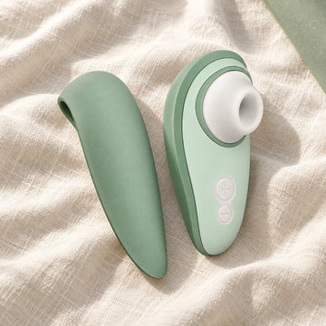 Womanizer Liberty 2 en verde salvia con su tapa de viaje sobre un tejido marfil