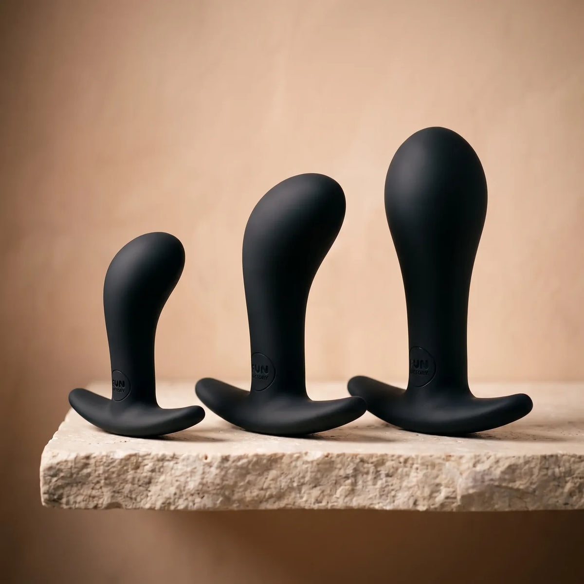 Trois petits objets en silicone de tailles croissantes sur pierre claire.