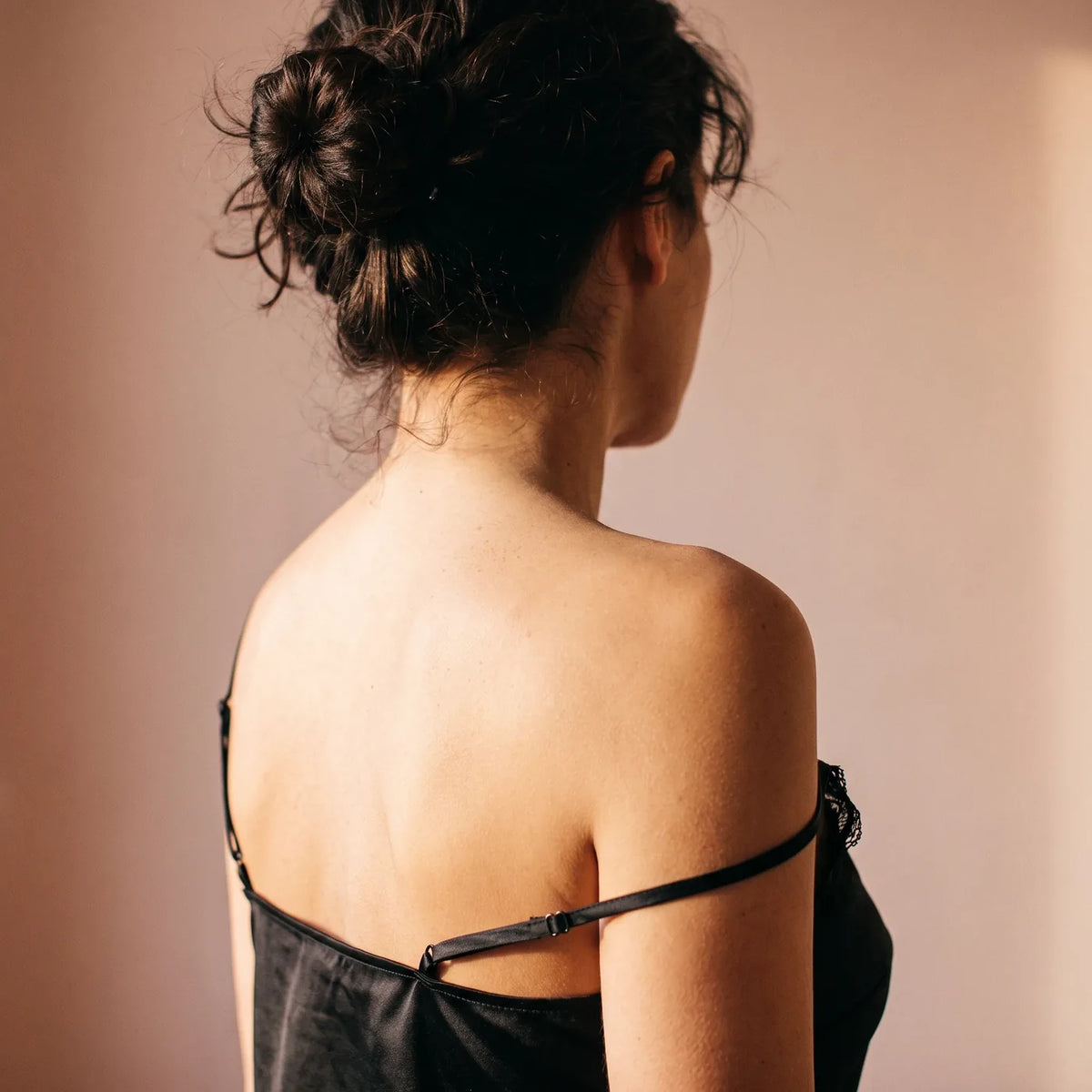 Épaule et nuque d'une femme, bretelle de nuisette en satin qui glisse.