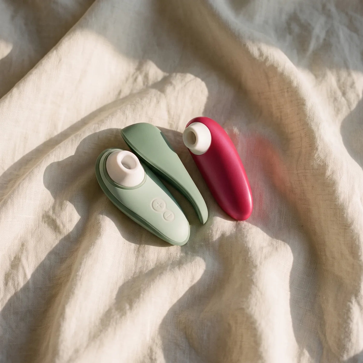 Deux stimulateurs Womanizer sur du lin ivoire.