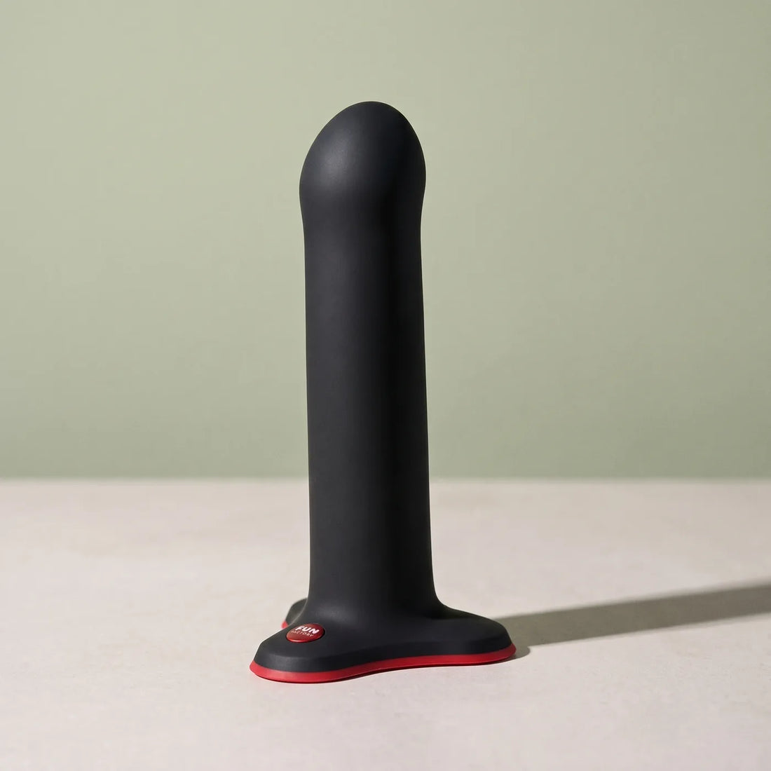 Sculpture en silicone noir et rouge FUN FACTORY Magnum, debout sur pierre claire.