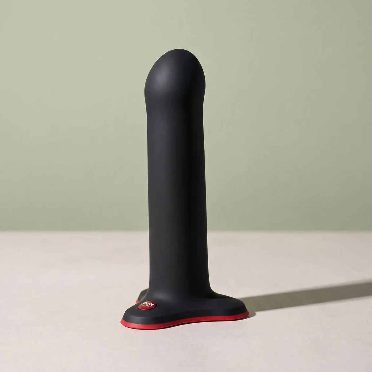 Sculpture en silicone noir et rouge FUN FACTORY Magnum, debout sur pierre claire.