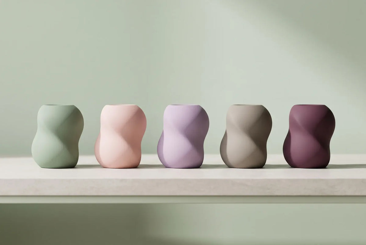Objets de design en silicone aux couleurs douces alignés sur une tablette de pierre claire.