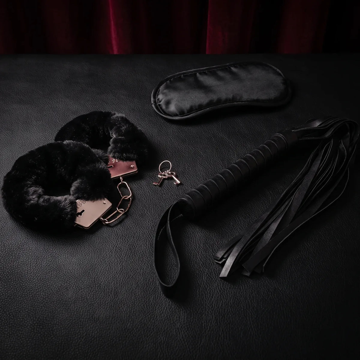 Menottes gainées de fourrure noire, bandeau et martinet noirs réunis sur cuir noir.