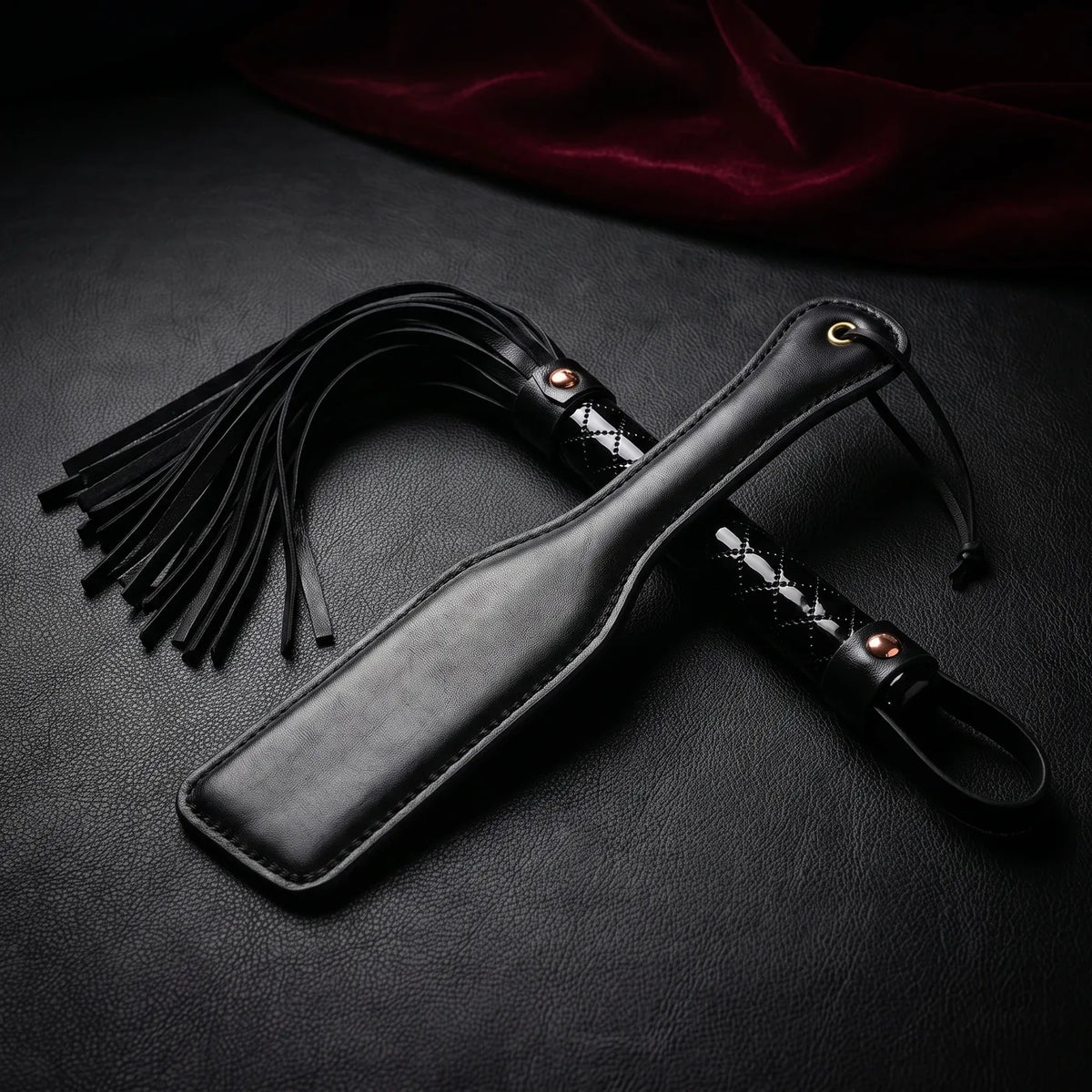 Martinet à lanières noires et paddle noir croisés sur cuir noir.