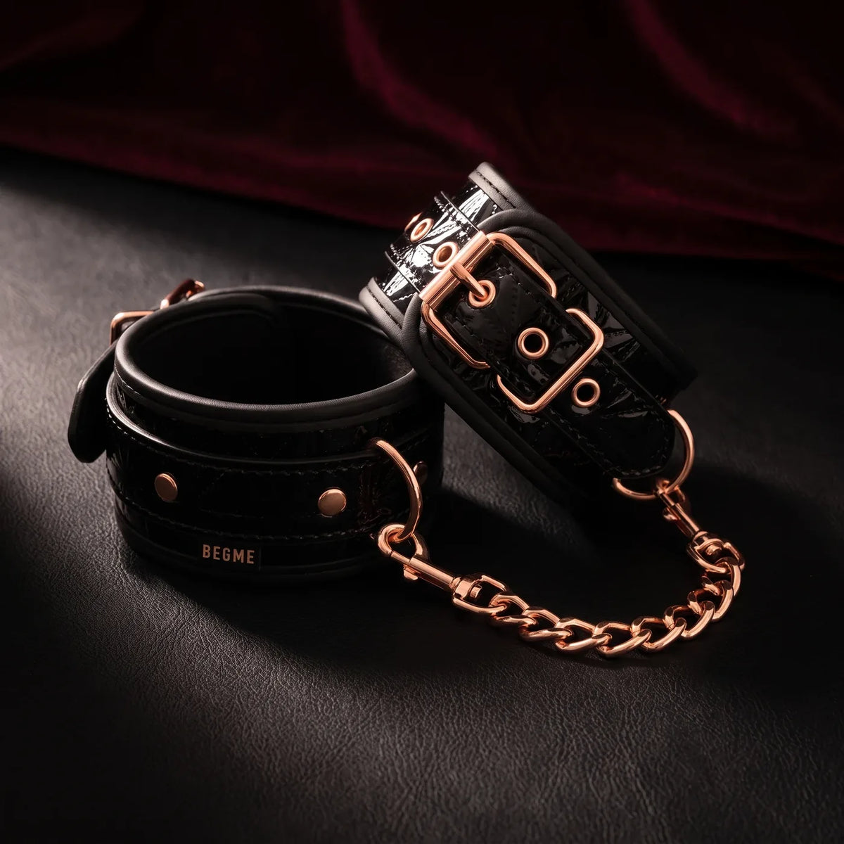 Paire de bracelets vernis noirs à boucles or rose reliés par une chaîne, sur cuir noir.