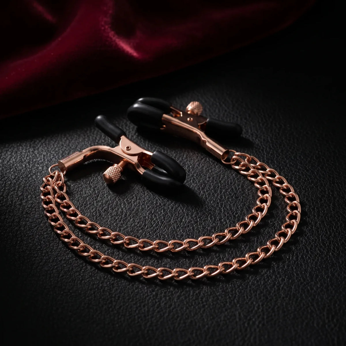 Paire de pinces réglables or rose reliées par une double chaîne, sur cuir noir.